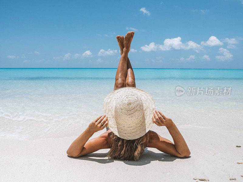 年轻女子在热带海滩晒太阳，翘着脚