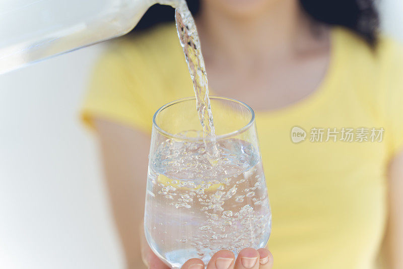 喝水。女人的手把新鲜的纯净水从水罐倒进杯子里。健康与饮食概念。健康的生活方式。医疗和美丽。Hydratation。