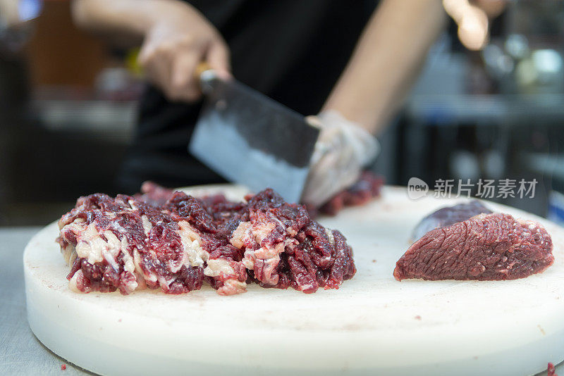 在一家牛肉火锅餐厅的开放式厨房里，厨师正在用刀切牛肉