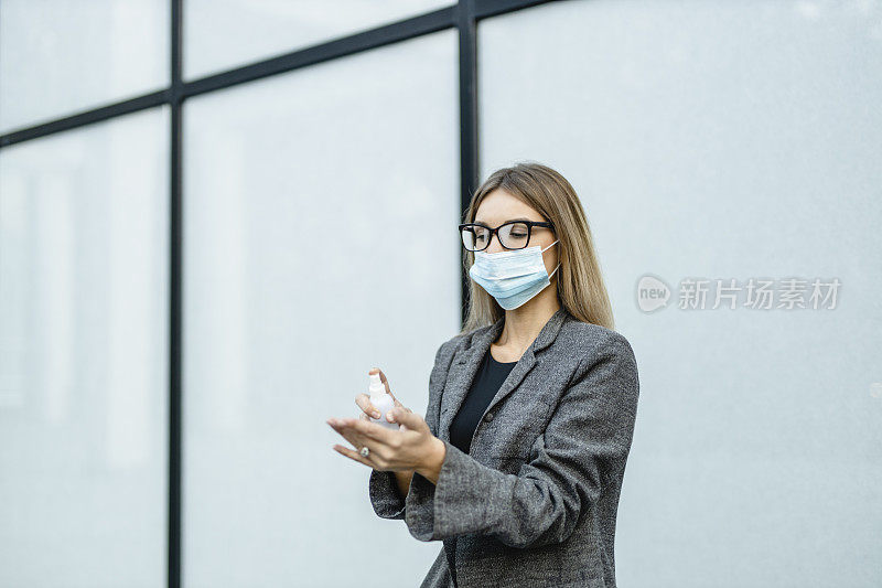 年轻女商人在冠状病毒大流行期间用洗手液洗手并佩戴防护口罩以保护自己