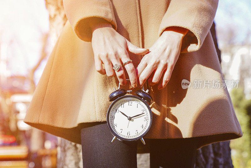 一个女人手里的黑色闹钟以自然为背景。