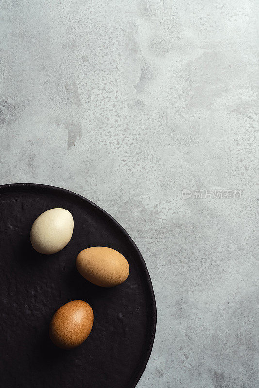 黑色的盘子上放着棕色的鸡蛋，背景是灰色