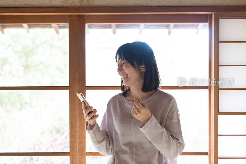 一名亚洲女性在室内手持智能手机并佩戴无线耳机麦克风。