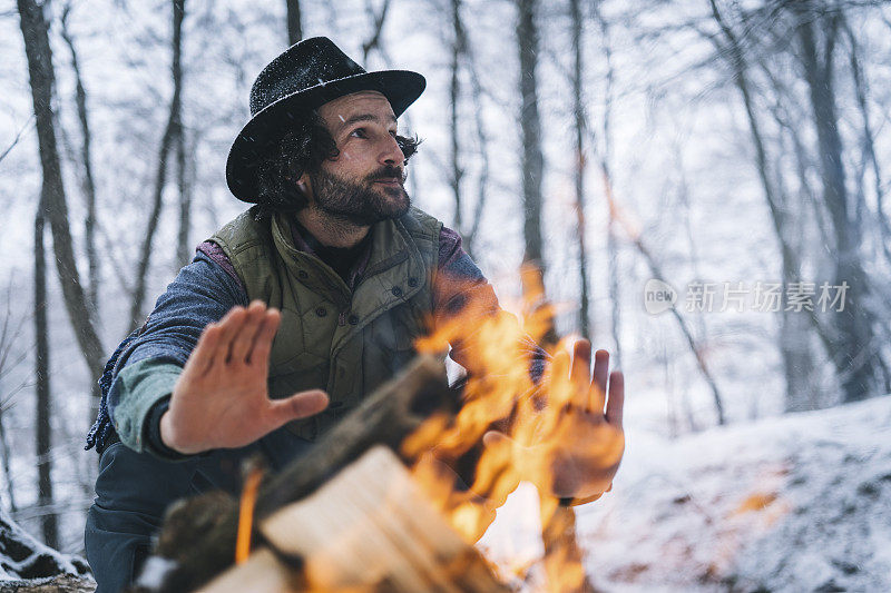清晨，在白雪皑皑的森林里，年轻人在篝火旁放松