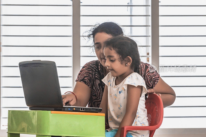 可爱的印度学校女孩与在线家教和母亲帮助在家学习