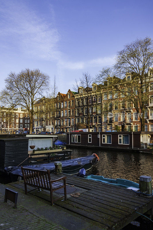 春天早晨的阿姆斯特丹，在晴朗的早晨天空下，到处都是房屋和船屋，绿树成荫的运河，桥上的砖砌人行道，到处都是历史。