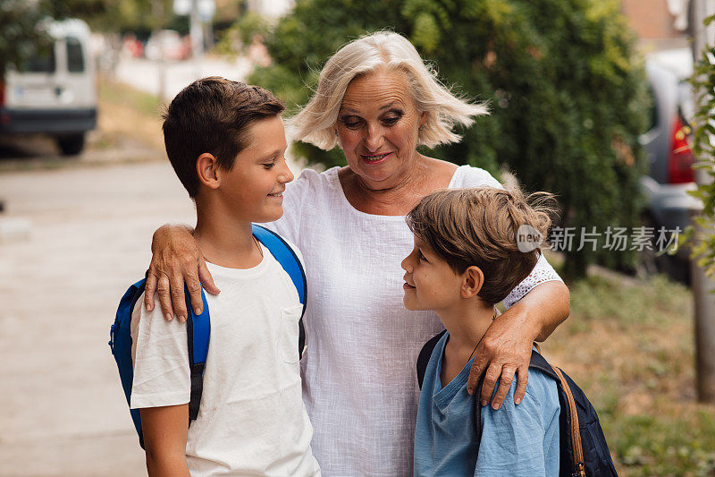 一位年长的成年妇女与她的孙子们拥抱和交谈。回到学校的概念。