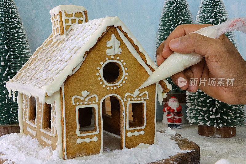 自制的姜饼屋被不认识的人用滚边袋的白色皇家糖霜装饰，展示在白雪覆盖的针叶林场景中，糖霜糖雪，模型冷杉树