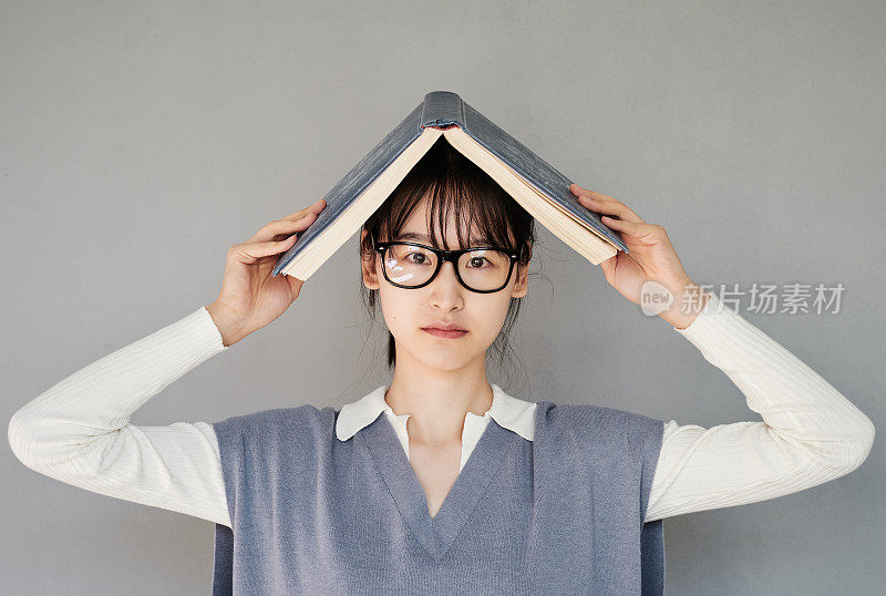 一幅被认认真真的亚洲女学生的肖像，戴着眼镜，头藏在书本下，背景孤立