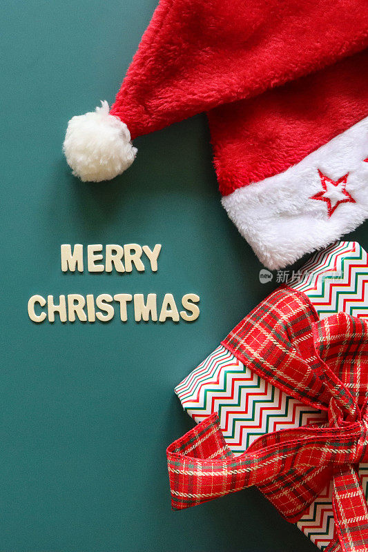 自制DIY简单的圣诞贺卡设计的图像，在青色背景上剪出白色字母，手工制作的节日圣诞贺卡，圣诞快乐的信息与圣诞老人的帽子和包装的礼物和鞠躬，复制空间