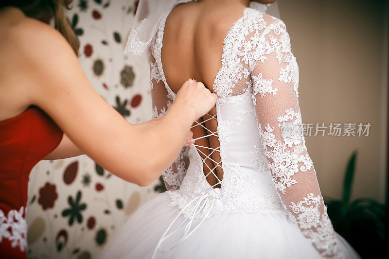伴娘帮助新娘穿上婚纱。