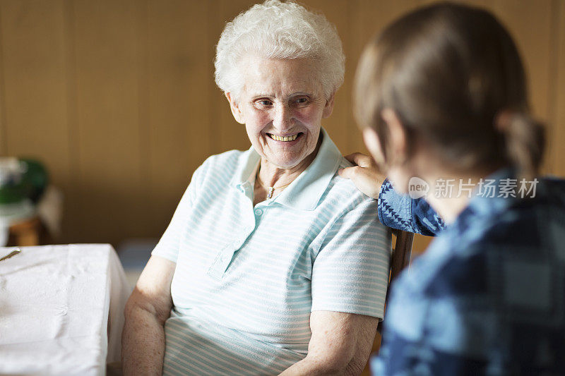 年轻的照顾者在家里支持一位老年妇女，抚摸她的肩膀