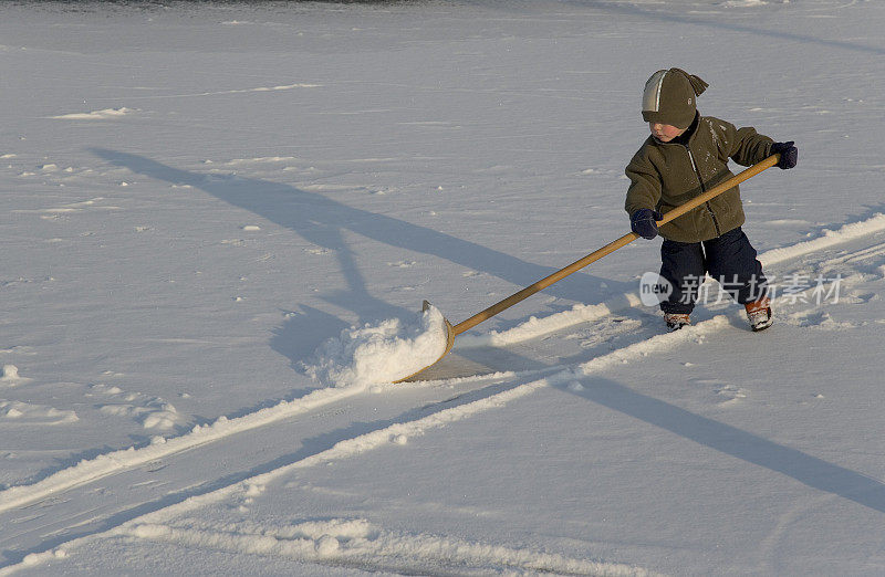 小男孩用雪铲在结冰的水池上工作(XL)