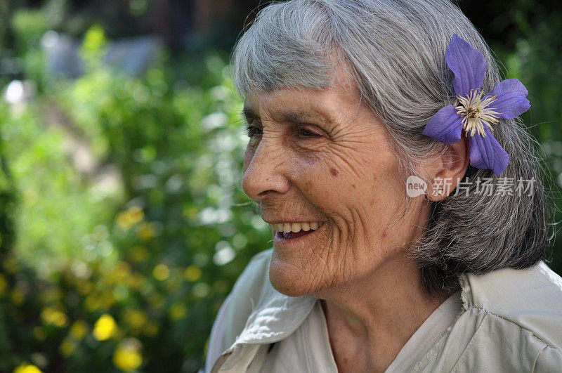 在花园里带着花的微笑的老妇人