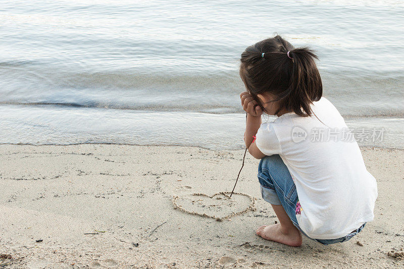 小女孩用棍子在沙滩上画了一颗心