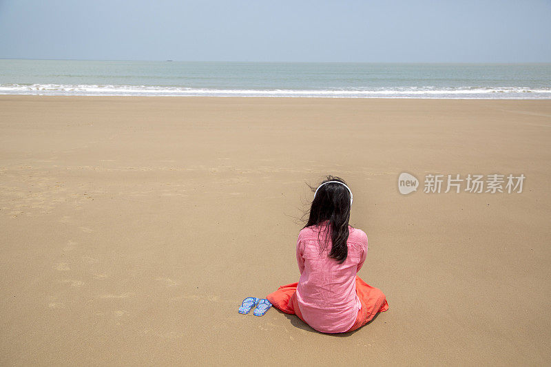 女孩坐在海滩上，听着音乐，面朝大海