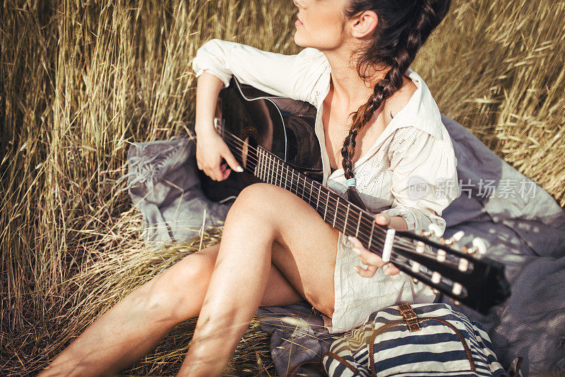 在草地上弹吉他的漂亮年轻女子