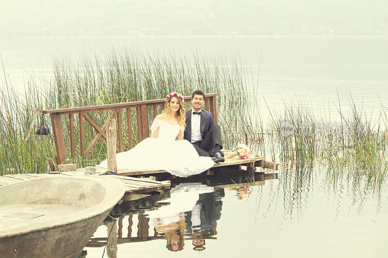 新娘和新郎坐在湖边的码头上