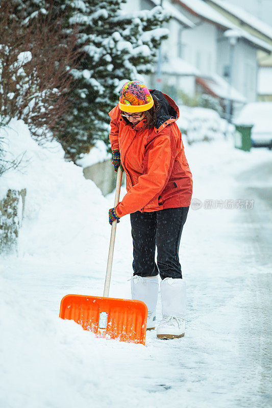 一个成熟的女人在清扫屋前的积雪