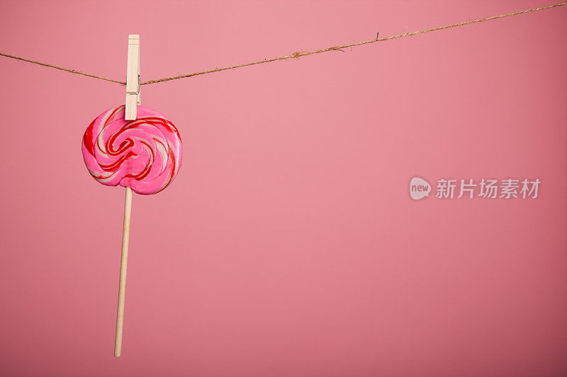 在粉红色背景下，挂在晾衣夹上的旋涡棒棒糖