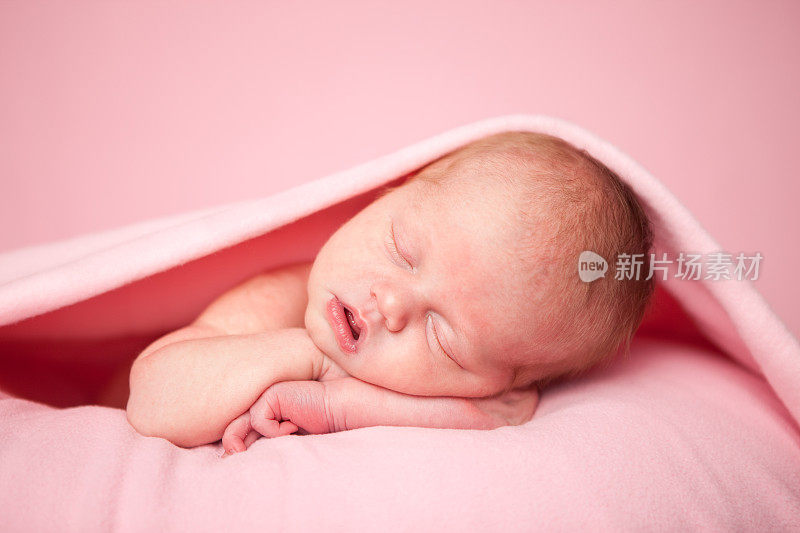 刚出生的女婴安静地睡在粉红色的毯子下