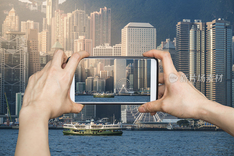 日出时分，一名女孩在香港维多利亚港用手机拍照