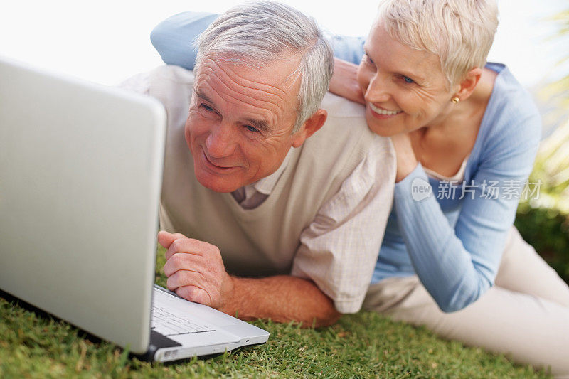 一对快乐的老夫妇在草地上使用笔记本电脑