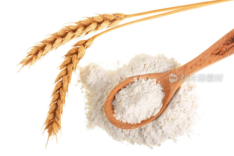 小麦穗和面粉堆在木勺孤立在白色的背景。前视图。平躺
