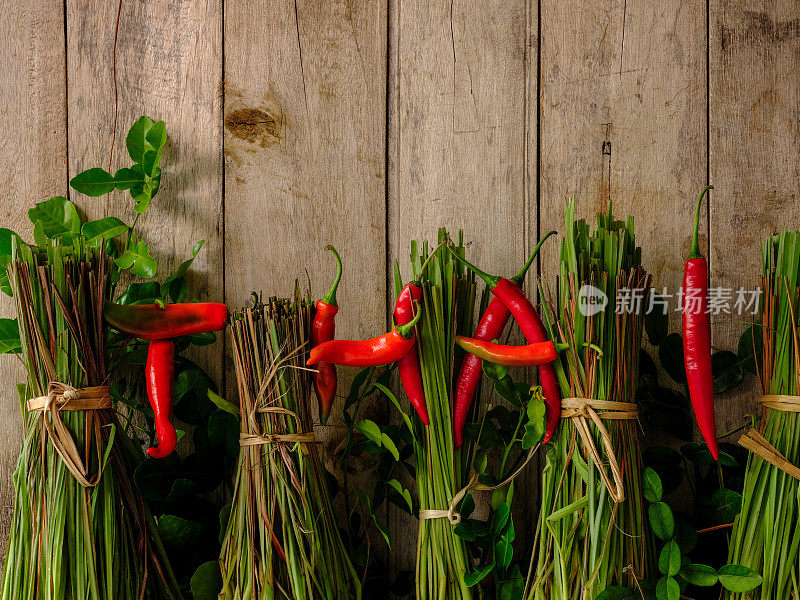 新鲜的泰国冬芋药草和香料映衬着古老的木质背景，在柠檬草中间用红辣椒写着“Thai”这个词。