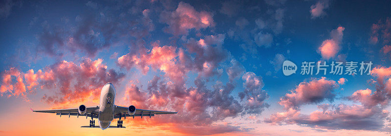 飞机和美丽的天空。落日时分，蓝天上布满了红、紫、橙三色的云雾，风景如画的客机正在飞翔。旅行。客运班机。商用飞机。私人飞机