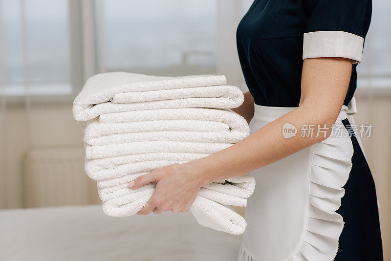 在酒店套房中，穿着制服的女佣拿着一堆干净的毛巾