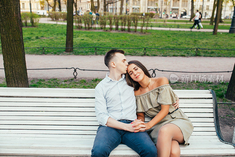 一对幸福相爱的年轻情侣坐在公园的长椅上拥抱