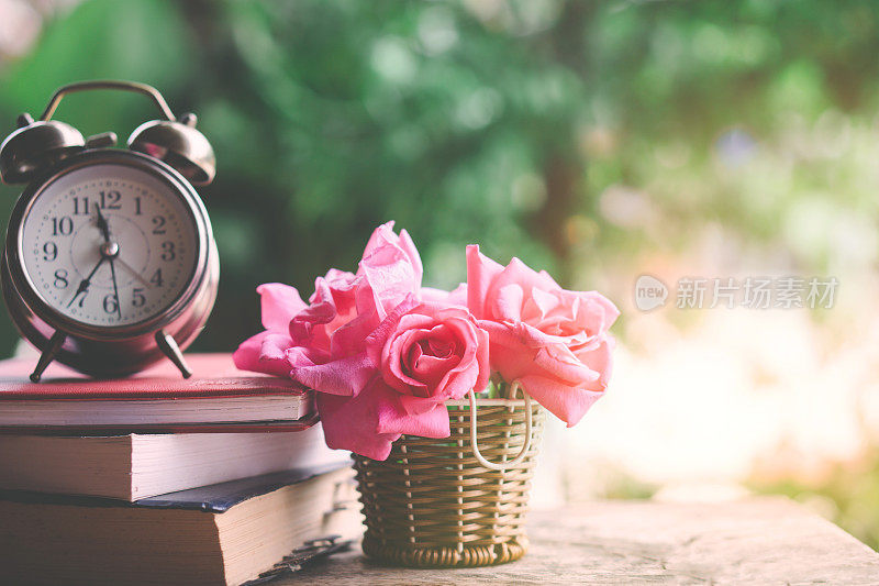 粉红色的玫瑰花束，时钟和书在木桌上自然的绿色花园