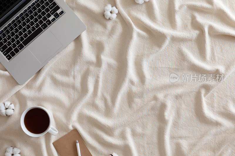 顶视图舒适的冬天背景与笔记本电脑，一杯茶与棉花花，温暖的针织毯子，女性复古的工作空间。生活方式的概念