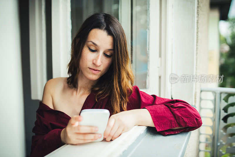 穿着红色衣服的女孩在窗户边拿着手机