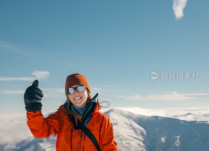 女性高山攀登者在山顶竖起大拇指