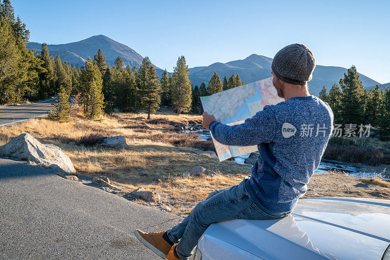 公路旅行概念;一名男子坐在汽车引擎盖上，在地图上查看方向