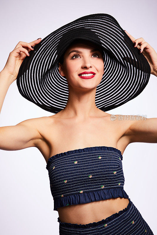 微笑的女人在拿着她的太阳帽边缘对着一个白色的背景