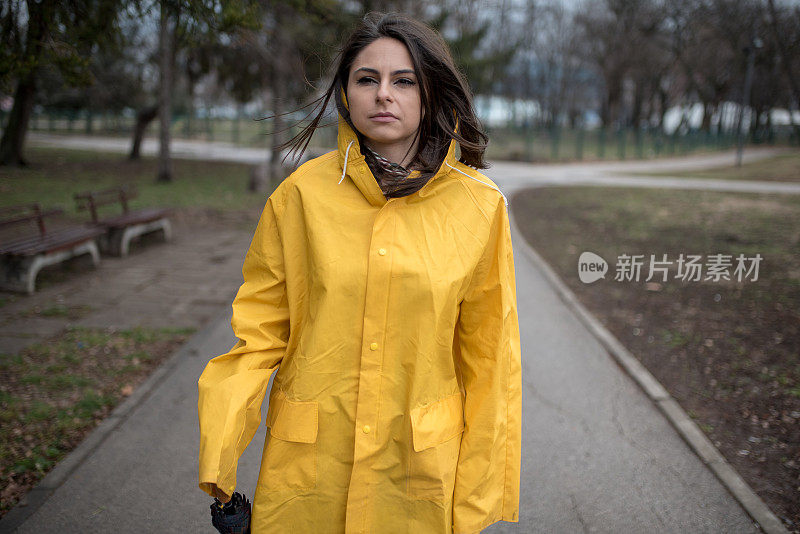 穿着黄色雨衣的年轻女子在公园里度过雨天