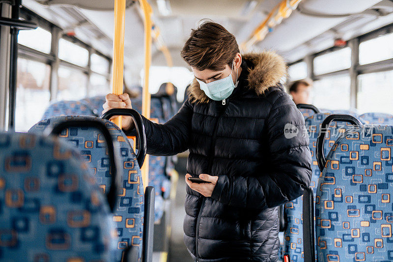 年轻男子站在公交车上，戴着消毒口罩，拿着手机