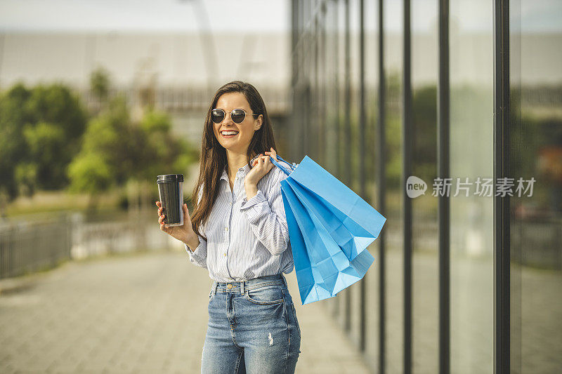 年轻漂亮的女人喝着咖啡，拎着购物袋走路