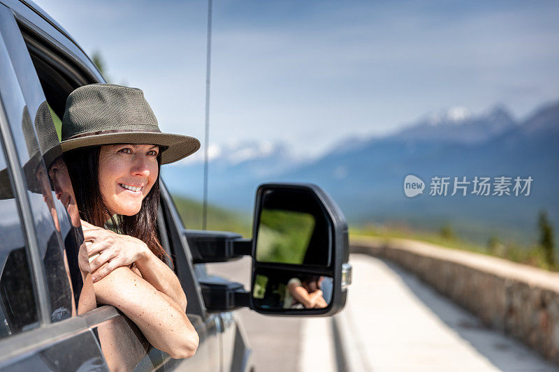 年轻时髦的女人靠在车窗上，一边开车一边欣赏风景