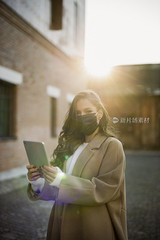 在冠状病毒大流行期间，佩戴防护口罩并在户外平板电脑上进行视频通话的妇女肖像