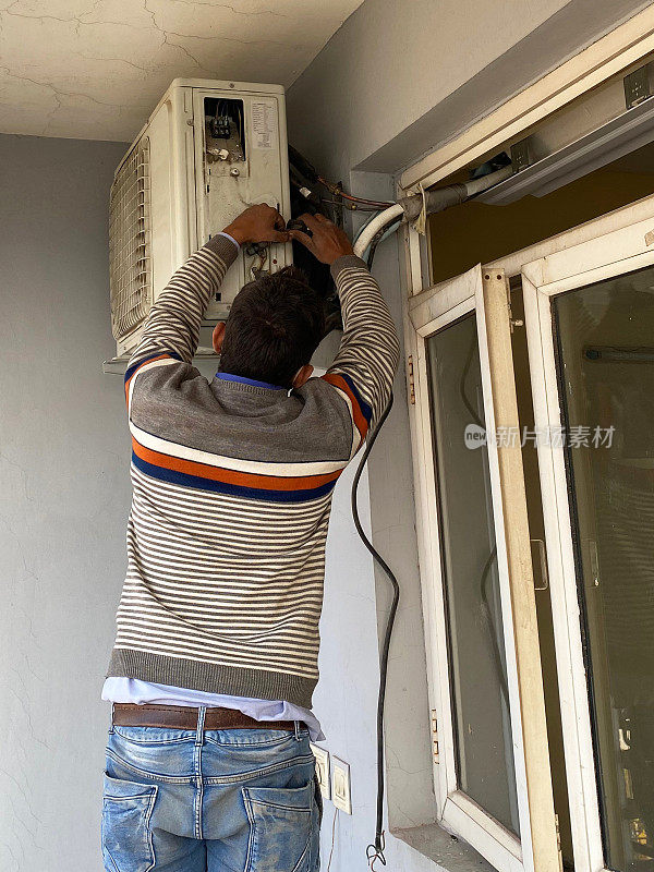 一个难以辨认的印度杂工在公寓阳台上安装空调排气装置