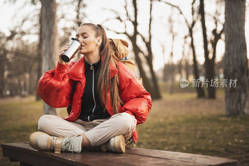 美丽的年轻女子喝着咖啡，在山间徒步旅行时休息一下