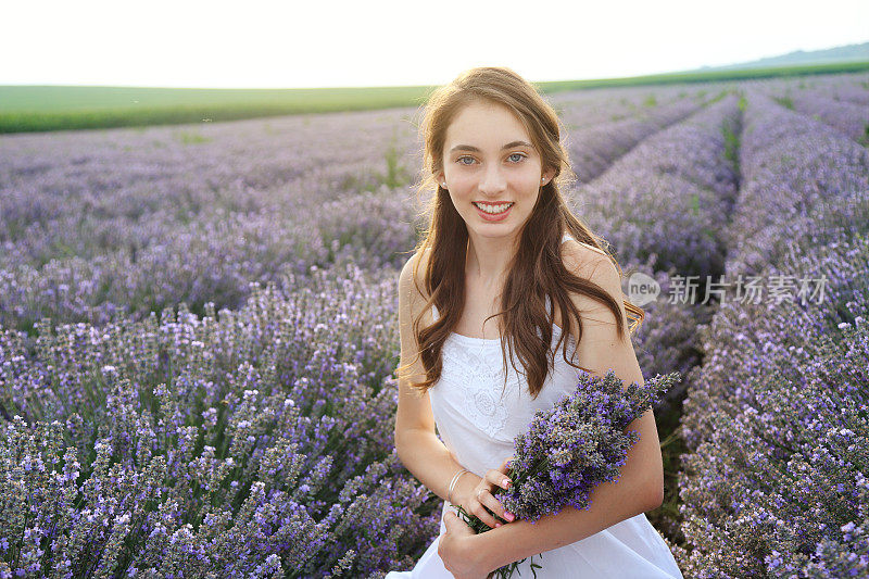 年轻的女孩在薰衣草地里捧着花束