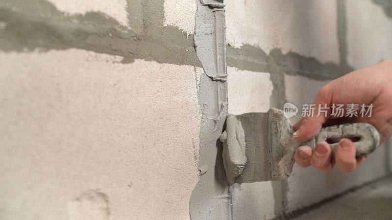 建筑工用泥铲把灰泥抹在混凝土墙上以固定金属建筑信标。建筑工用泥铲涂抹灰泥