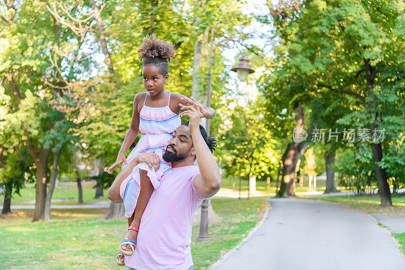 快乐的非裔美国父亲在公园里用肩膀扛着女儿玩耍。