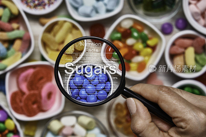 含糖食品的营养成分。俯视图的彩色软糖，棒棒糖，糖果和棉花糖与一个放大镜
