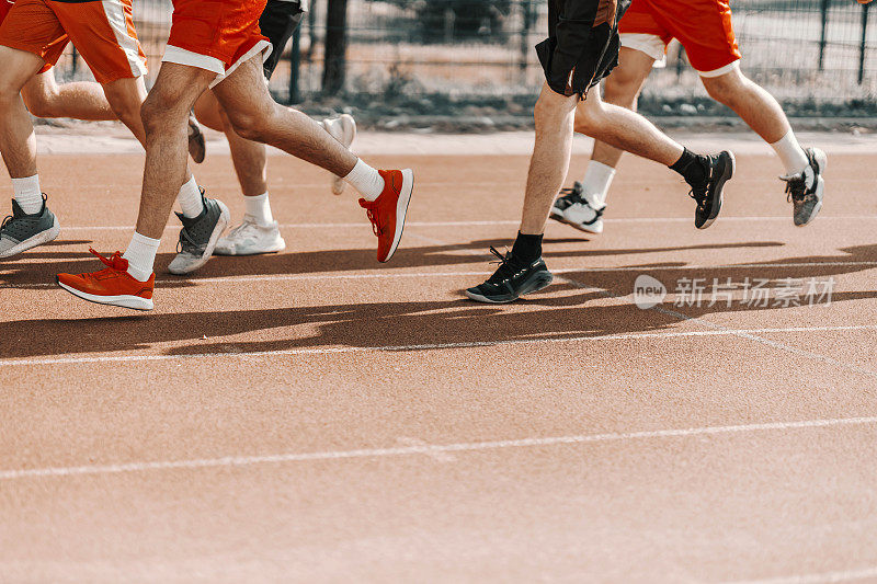 体育场内的一群跑步者。重点是一个男人的腿在跑道上跑步和热身肌肉。团体健身训练和健身马拉松